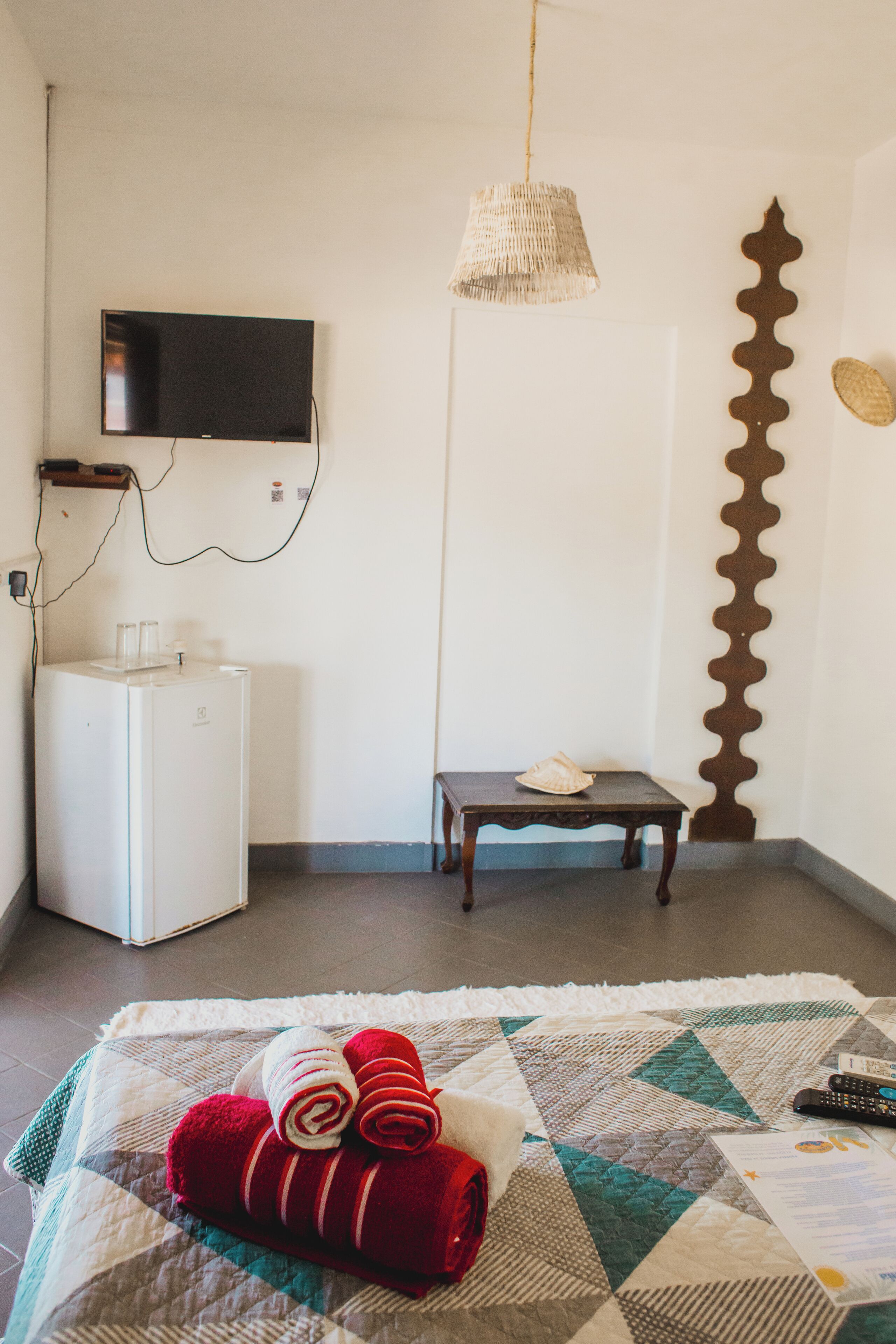 A room with a bed, a TV mounted on the wall, a small table, and a refrigerator.