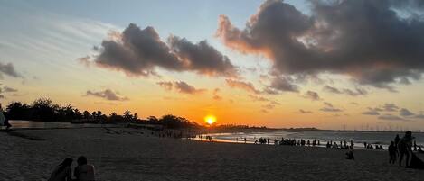 Uma praia ao pôr do sol com pessoas e um píer ao fundo.