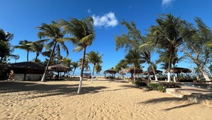 Un complexe hôtelier de bord de mer avec des bungalows aux toits de chaume, des palmiers et une plage de sable.
