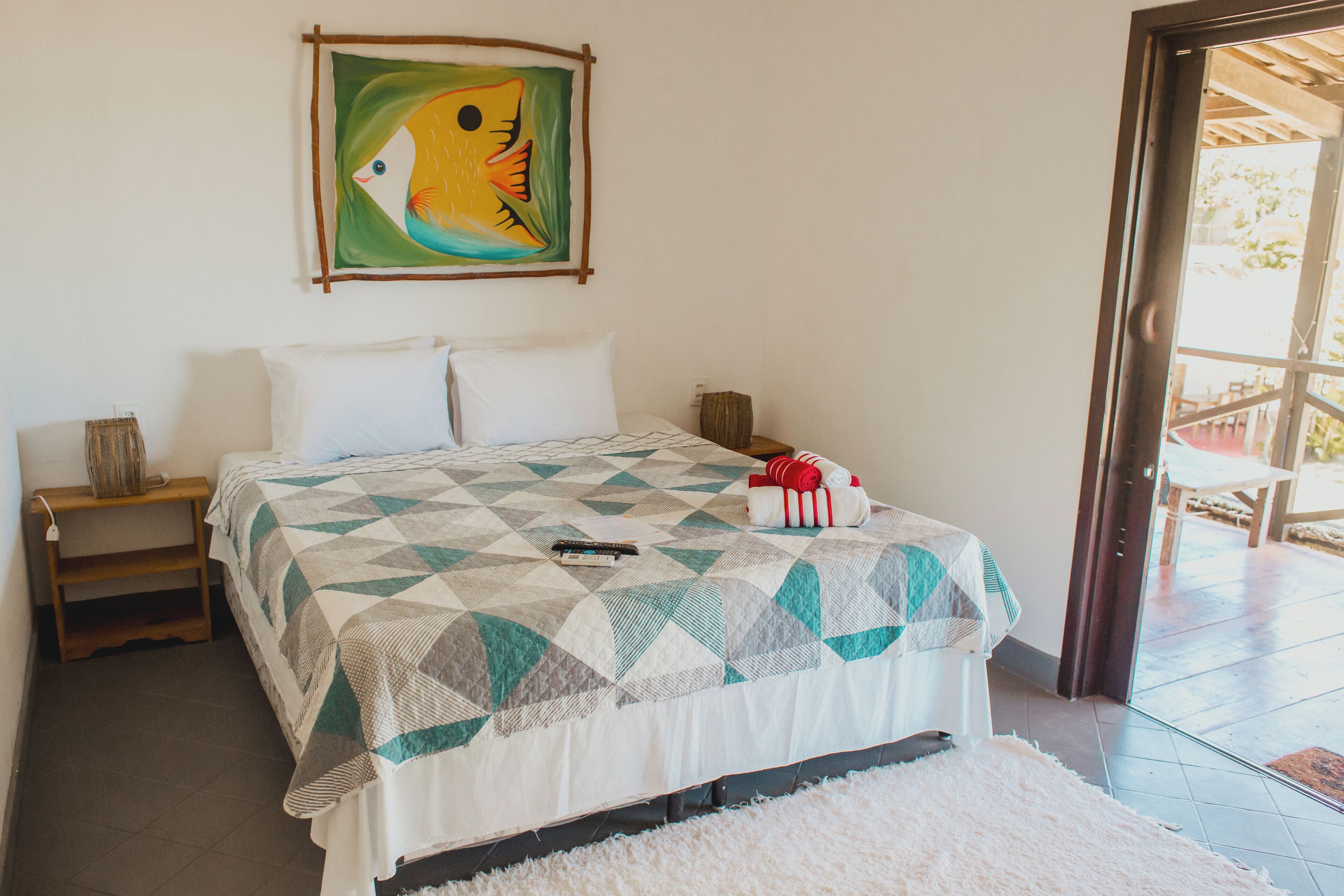 A bedroom with a bed, pillows, a blanket, a painting, a nightstand, and a door leading to an outdoor area.