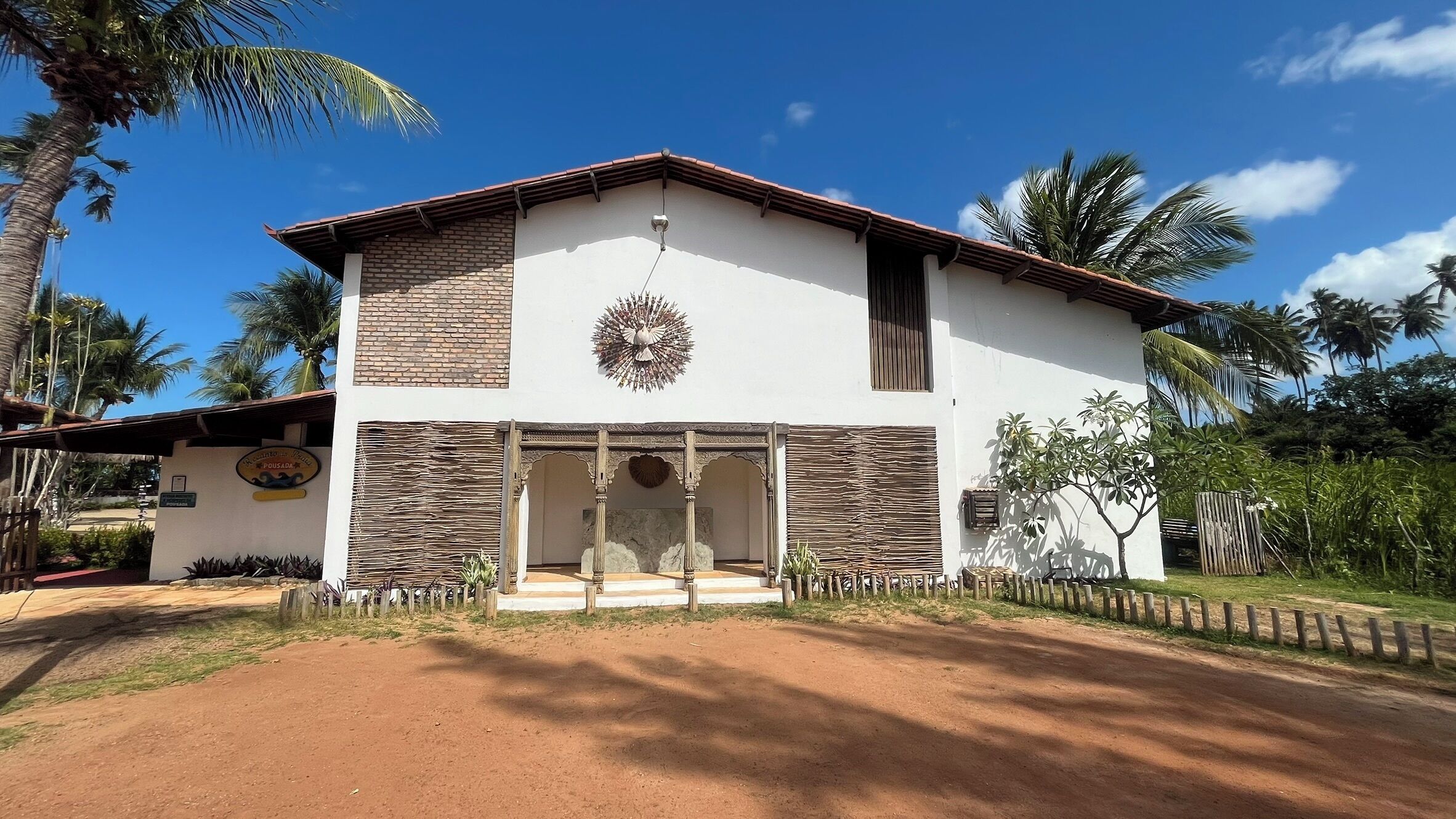 A two-story building with a white facade and stone accents, a decorative wall hanging, and a paved entrance area.