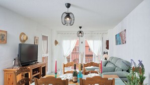 Un coin repas avec une table en bois dressée pour quatre personnes, un téléviseur posé sur un meuble et un canapé à l’arrière-plan.