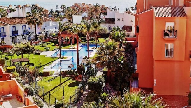 Un complexe hôtelier doté d’une piscine, de palmiers et offrant une vue sur la mer.