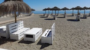 Une plage avec des bancs en bois peints en blanc et des parasols en chaume.