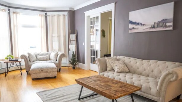 Ein Wohnzimmer mit einem beigen Sofa, passendem Hocker und einem Couchtisch aus Holz.