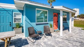A two-story house with a blue exterior, a red door, and a small porch with two wicker chairs and a table. - 60 Seconds to Sand (Ormond Beach)
