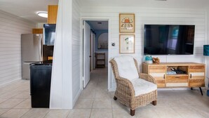 A modern living room with a large flat-screen TV, a wicker chair, and a wooden cabinet. - 60 Seconds to Sand (Ormond Beach)