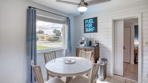 A dining area with a round table and chairs, a ceiling fan, and a neon sign on the wall. - 60 Seconds to Sand (Ormond Beach)