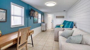 A room with a dining table and chairs, a sofa, and a TV mounted on the wall. - 60 Seconds to Sand (Ormond Beach)
