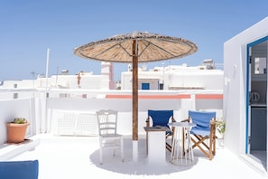 Une terrasse sur le toit, avec une table, des chaises et un parasol en paille.