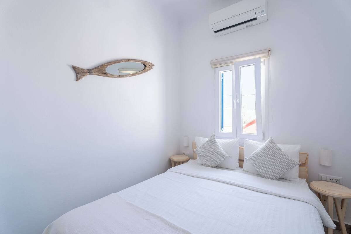 Un dormitorio con una cama, dos mesitas de noche, una ventana y un aire acondicionado instalado en la pared.