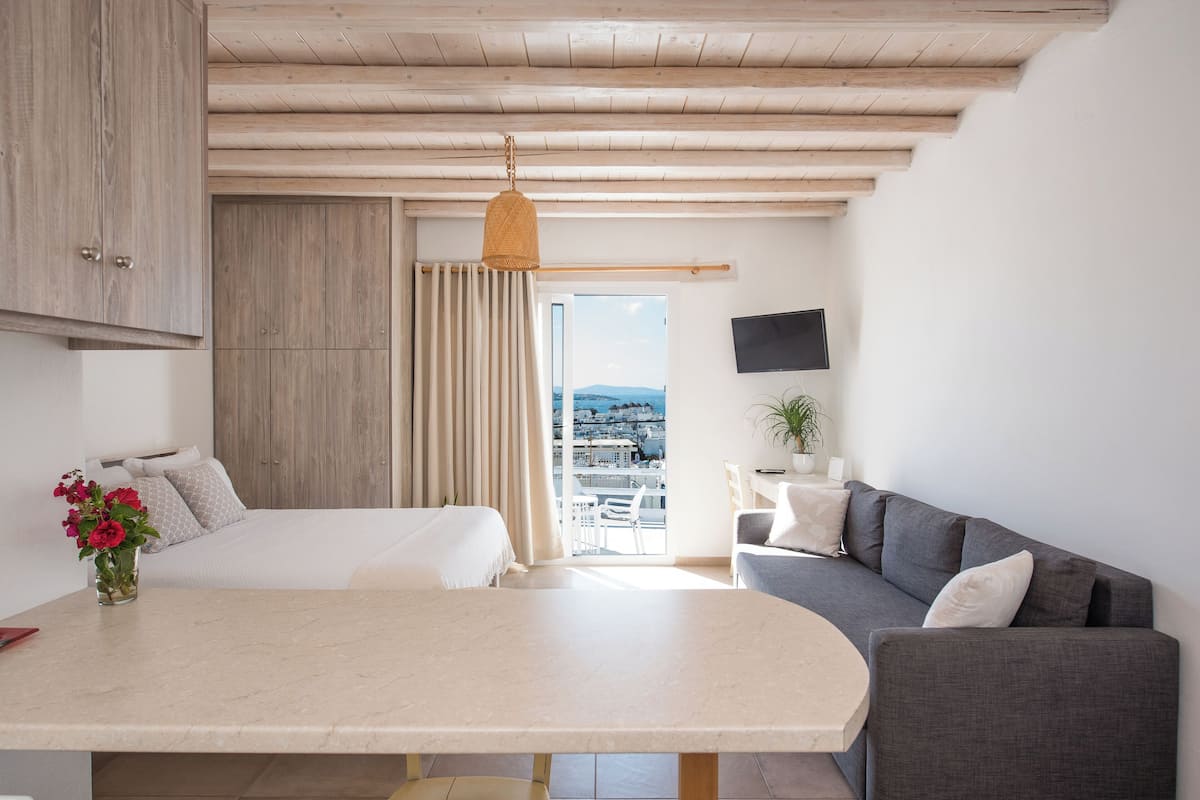 Una habitación de hotel moderna con cama, sofá, mesa de comedor y balcón con vista a la ciudad.