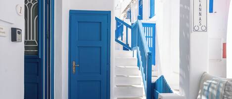 A hallway with a blue door, a staircase with blue railings, and a blue table with fruit.