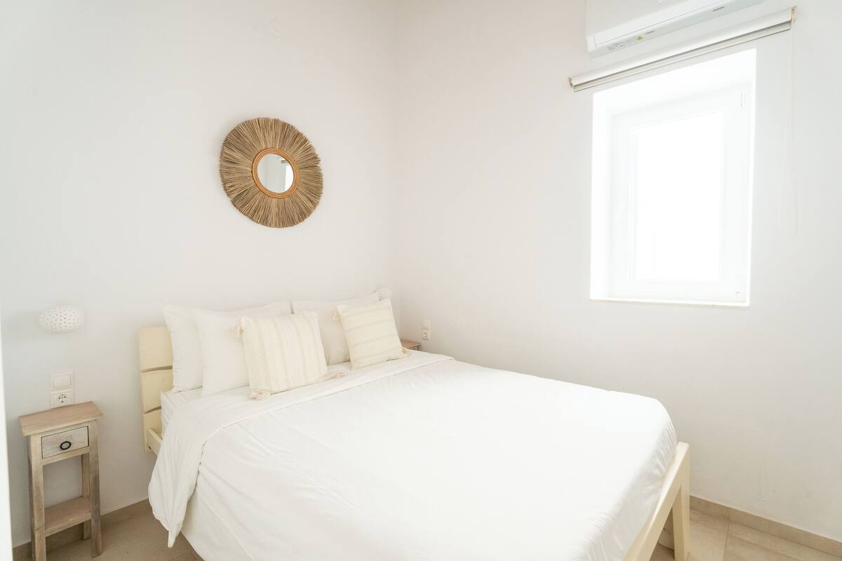 Un dormitorio minimalista con una cama, una mesita de noche y un espejo redondo en la pared.