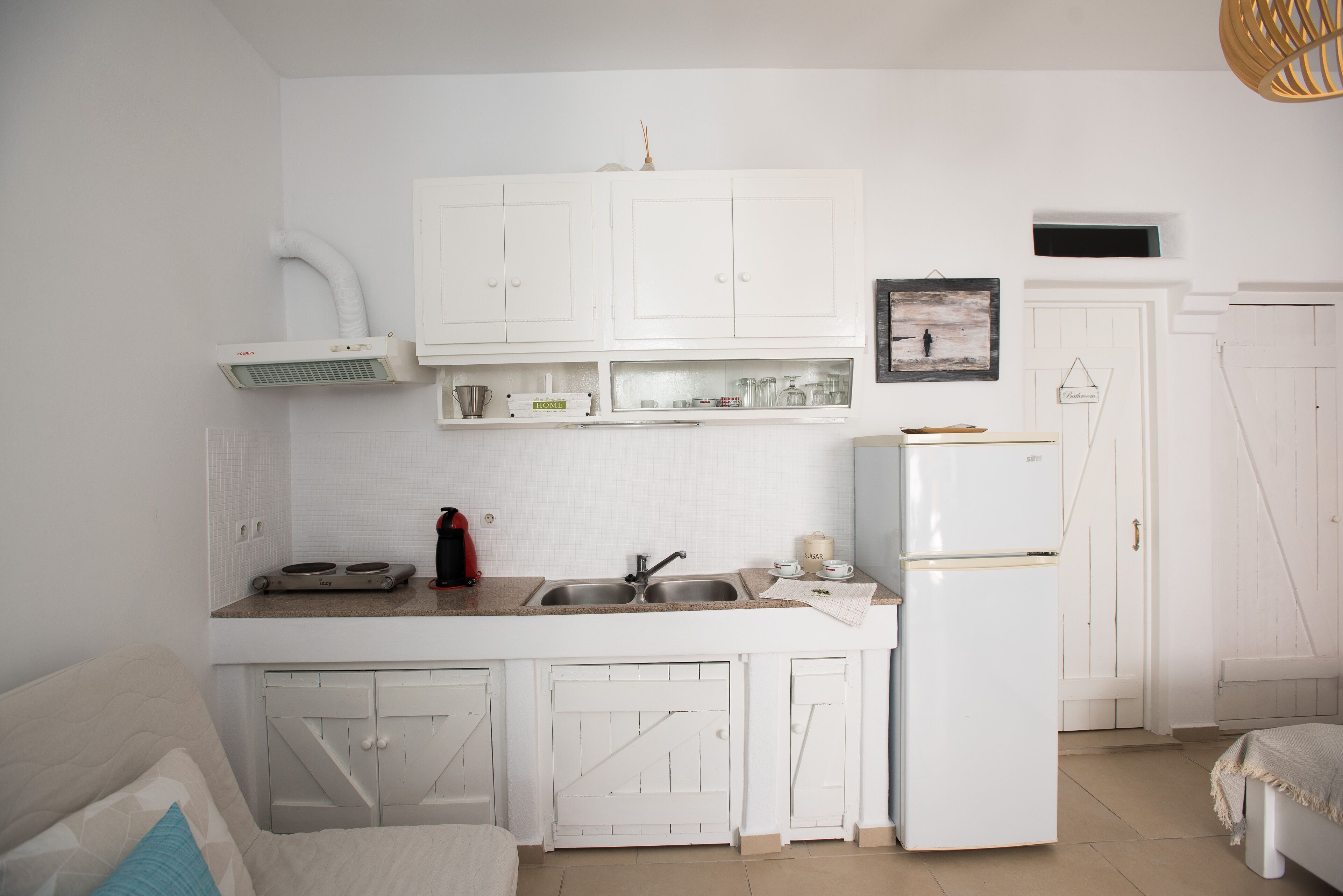 A compact kitchen with white cabinets, a built-in oven, a refrigerator, and a sink.
