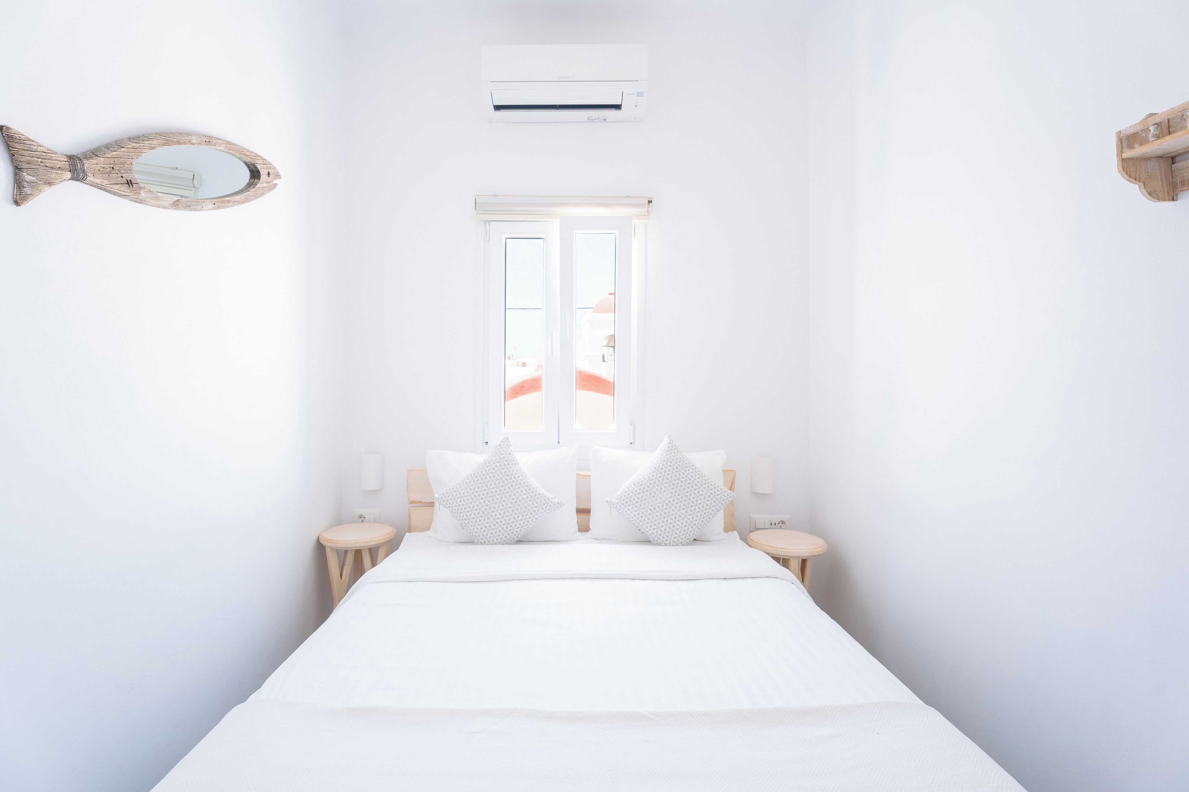 Quarto de hotel minimalista com uma cama grande, duas mesas de cabeceira, uma janela com vista, um ar condicionado e um espelho fixado na parede.