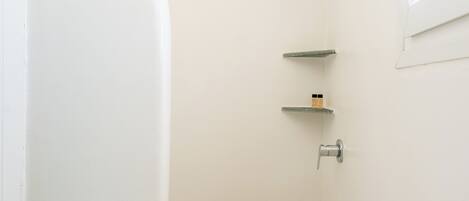 A small, white bathroom with a shower, a window, and a tiled floor.