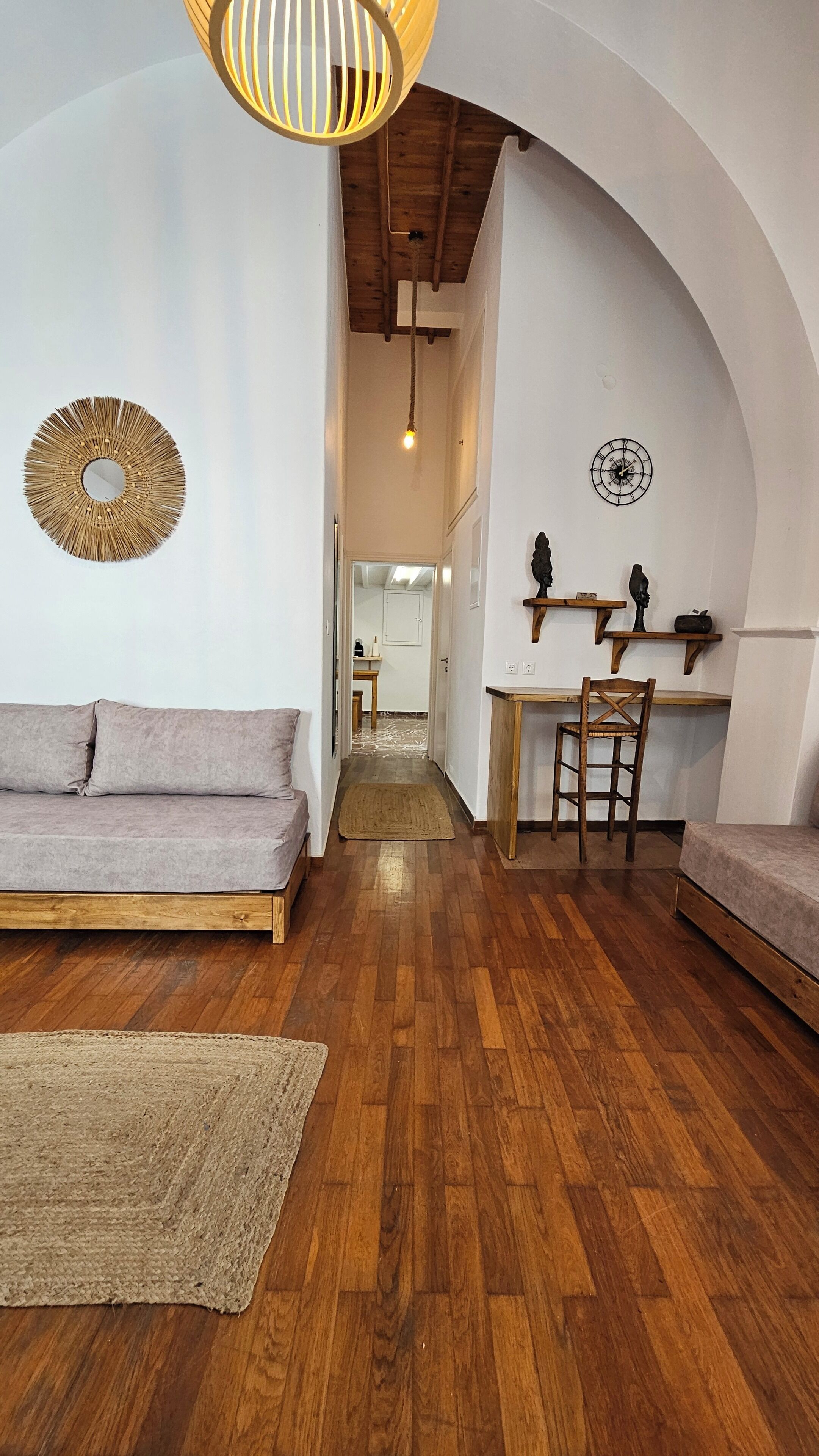 Una habitación acogedora con piso de madera, un sofá, una mesita con sillas y una lámpara colgante.