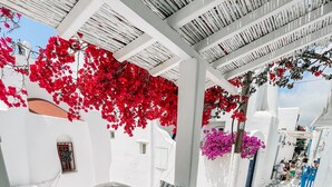 A white-walled room with a blue sofa and a round table, featuring a stone-patterned floor and a view of a narrow street. - Eleanna's Mykonos (Mykonos)