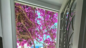 A door leading to a balcony with a view of a building and a tree with pink flowers. - Eleanna's Mykonos (Mykonos)