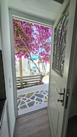 Uma porta que dá para uma varanda com vista para um edifício e uma árvore com flores rosa.