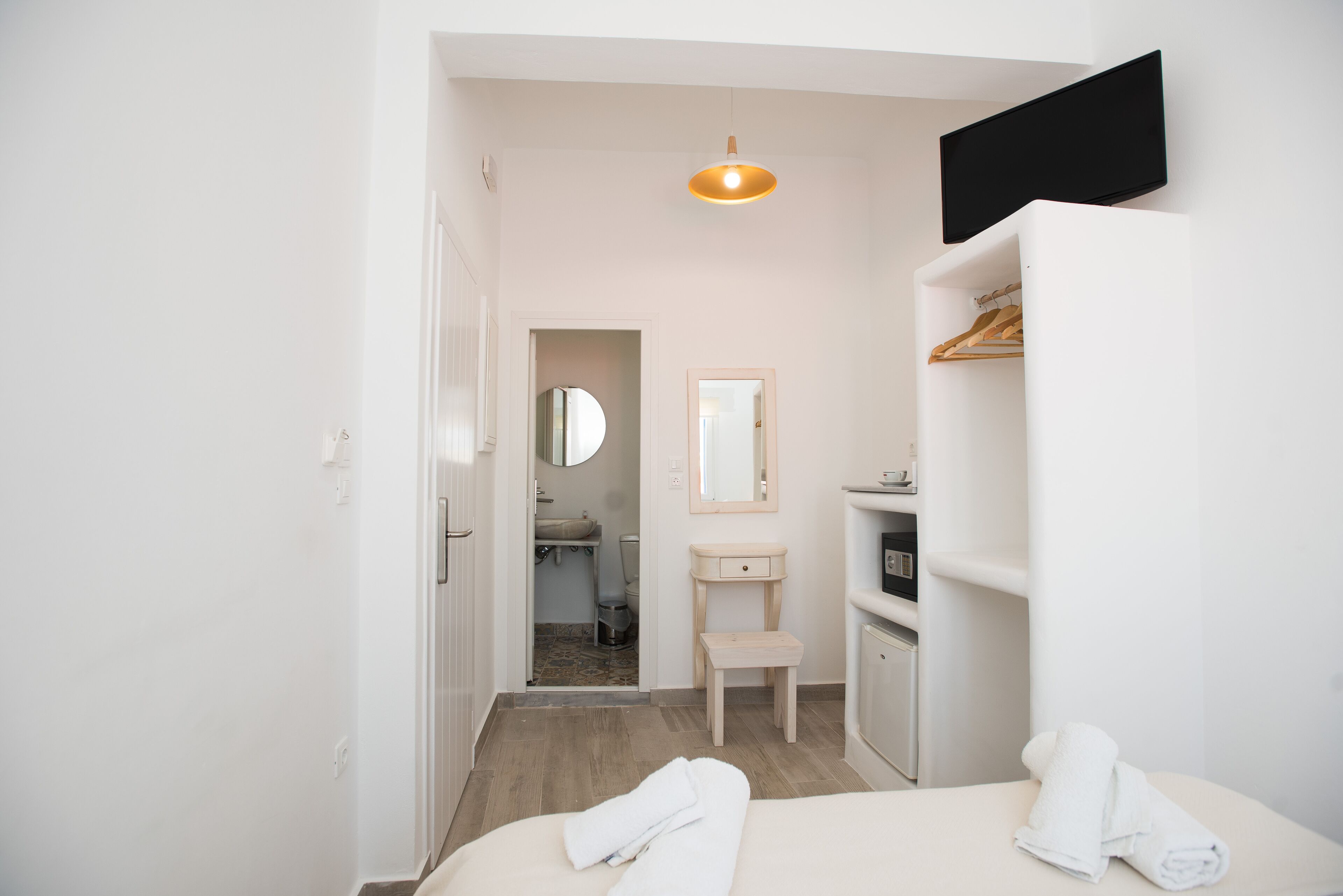 A hotel room with a bed, a bedside table, a mirror, a wardrobe, and a bathroom visible through an open door.