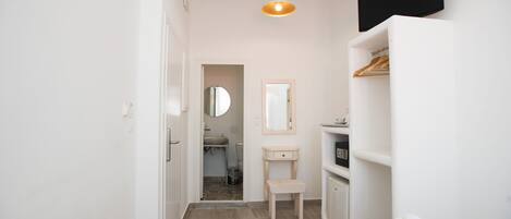 A hotel room with a bed, a bedside table, a mirror, a wardrobe, and a bathroom visible through an open door.