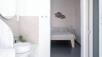 Un baño moderno con lavamanos y espejo blancos, y una cama en la habitación contigua.