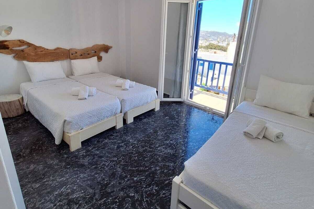 Una habitación con dos camas, cabecero de madera, un ventanal grande y un balcón.