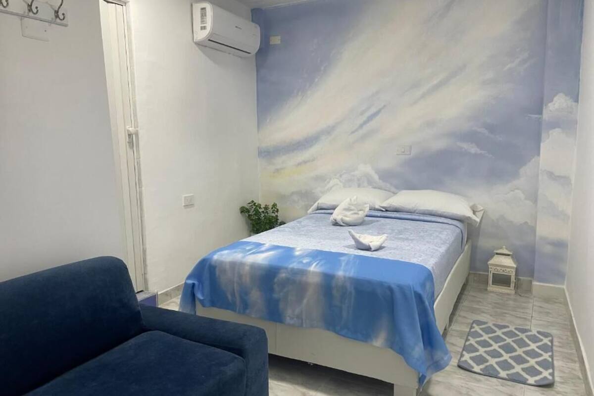 A bedroom with a bed, a blue sofa, a small plant, and a decorative wall mural.