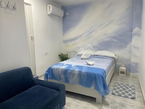 Una camera da letto con un letto, un divano blu, una piccola pianta e un murale decorativo.