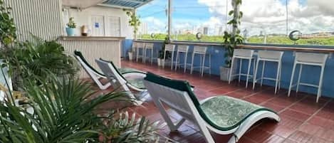Un espacio al aire libre cubierto con sillas y mesas, piso de baldosas y plantas en macetas.