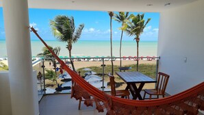 A balcony with a view of the beach, a hammock, a table, and chairs. - Miramar Na Praia (João Pessoa)