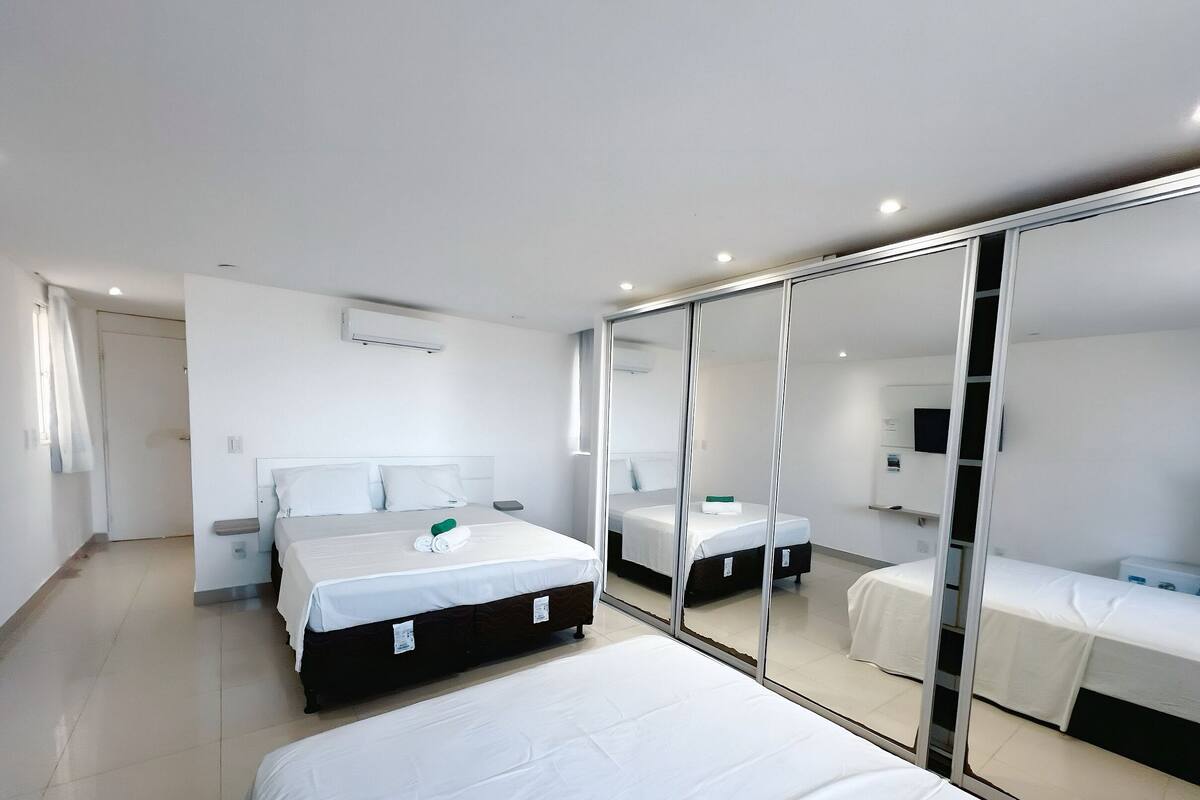 A modern hotel room with a large bed, a separate sleeping area, a mirror, and a flat-screen TV.