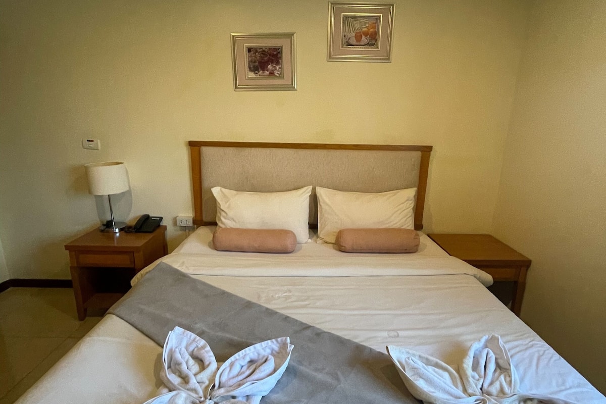 A hotel room with a large bed, two nightstands, a lamp, and two framed pictures on the wall.