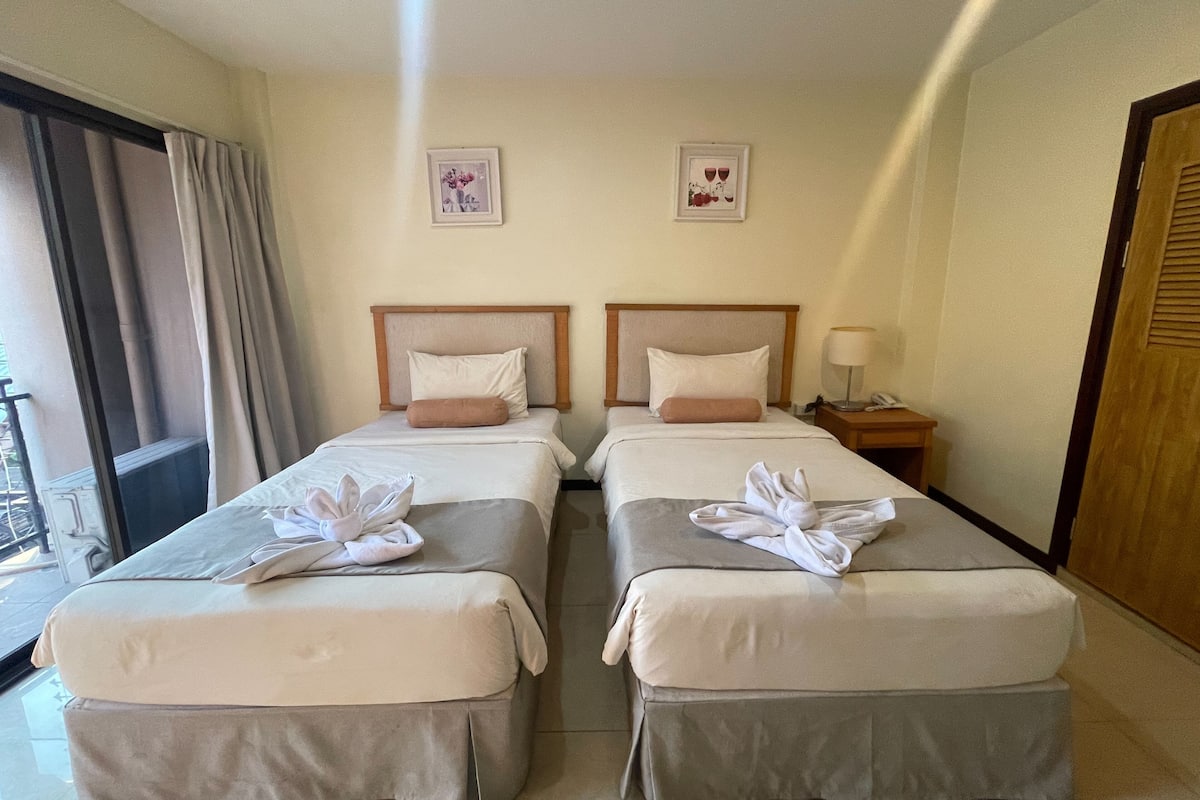 A hotel room with two beds, each with a headboard, a bedside table with a lamp, and two framed pictures on the wall.