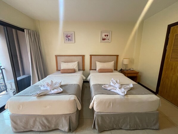 Habitación de hotel con dos camas, cada una con cabecero, mesita de noche con lámpara y dos cuadros en la pared.
