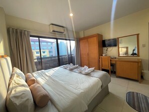 Habitación de hotel con una cama grande, un escritorio, un armario, un televisor y una ventana con cortinas.