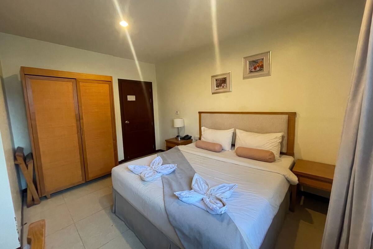 A hotel room with a bed, two nightstands, a wooden wardrobe, and a door.
