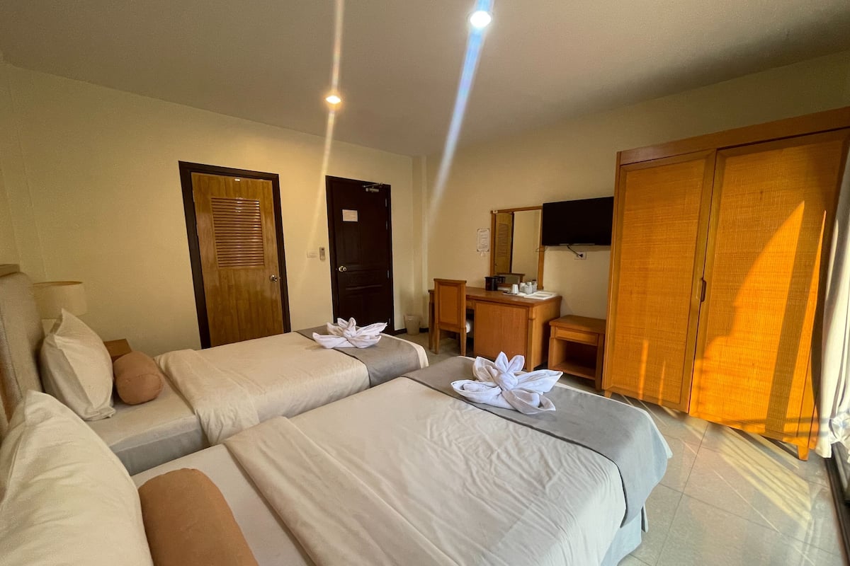 A hotel room with two beds, a desk, a chair, a television, and a wardrobe.