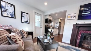 A living room with a sofa, coffee table, and fireplace. There is a kitchen in the background. - Adorable 1 BR on the mount (Pittsburgh)