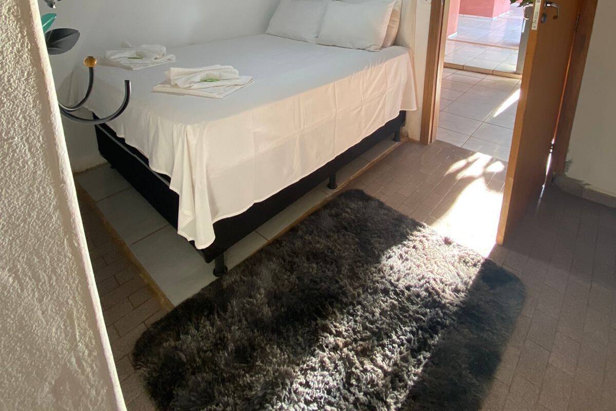 Une chambre à coucher comprenant un lit, un ventilateur de plafond, une fenêtre avec des rideaux et une porte donnant sur une autre pièce.