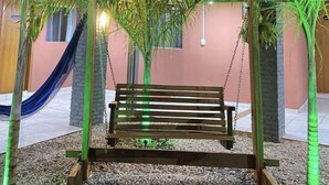 A wooden swing under a green canopy, surrounded by palm trees and a hammock.