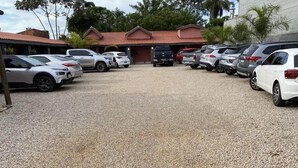 A parking lot with several cars parked in rows, a building with a red roof in the background, and trees surrounding the area.