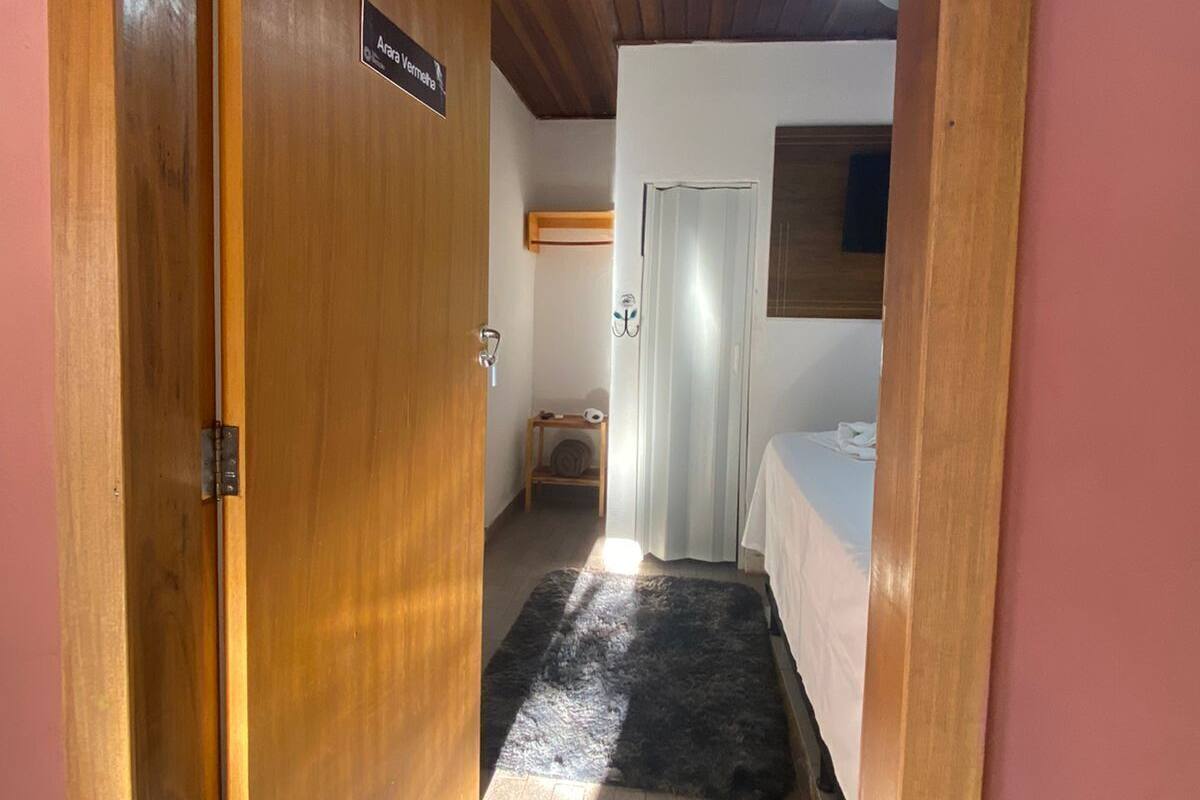 Un couloir étroit avec une porte en bois portant l’inscription « Aram Vemera », qui donne sur une pièce contenant un lit et un ventilateur de plafond.