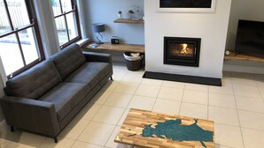 A modern living room with a gray sofa, a wooden coffee table, a fireplace, and a large window.