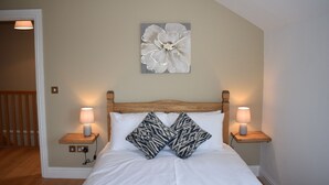 A bedroom with a wooden headboard, two bedside lamps, a white bedspread, and a large floral artwork on the wall.