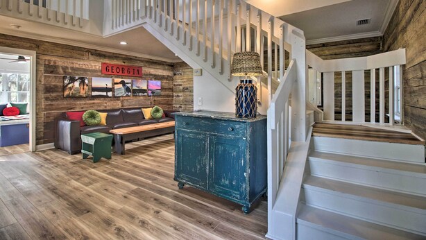 A spacious living area with a wooden staircase, a green cabinet, and a sofa with colorful cushions. - Waterfront, 7 acres; Stunning Home on Coastal Tidal Marsh w/Private Dock (Shellman Bluff)
