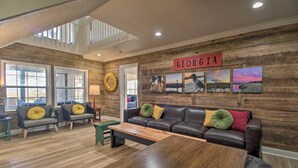 A spacious living room with a wooden wall, a leather sofa, and a coffee table. - Waterfront, 7 acres; Stunning Home on Coastal Tidal Marsh w/Private Dock (Shellman Bluff)