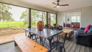 A covered outdoor area with a table and chairs, a wooden bench, and a sofa with cushions. - Waterfront, 7 acres; Stunning Home on Coastal Tidal Marsh w/Private Dock (Shellman Bluff)